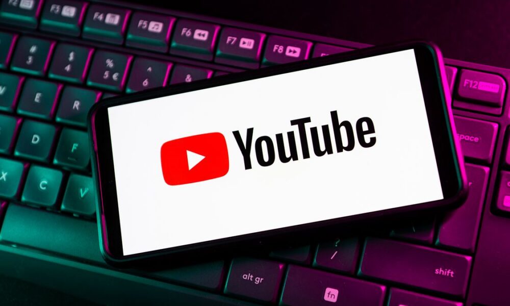 Logo YouTube sur smartphone pos&eacute; sur clavier d'ordinateur r&eacute;tro&eacute;clair&eacute;.
